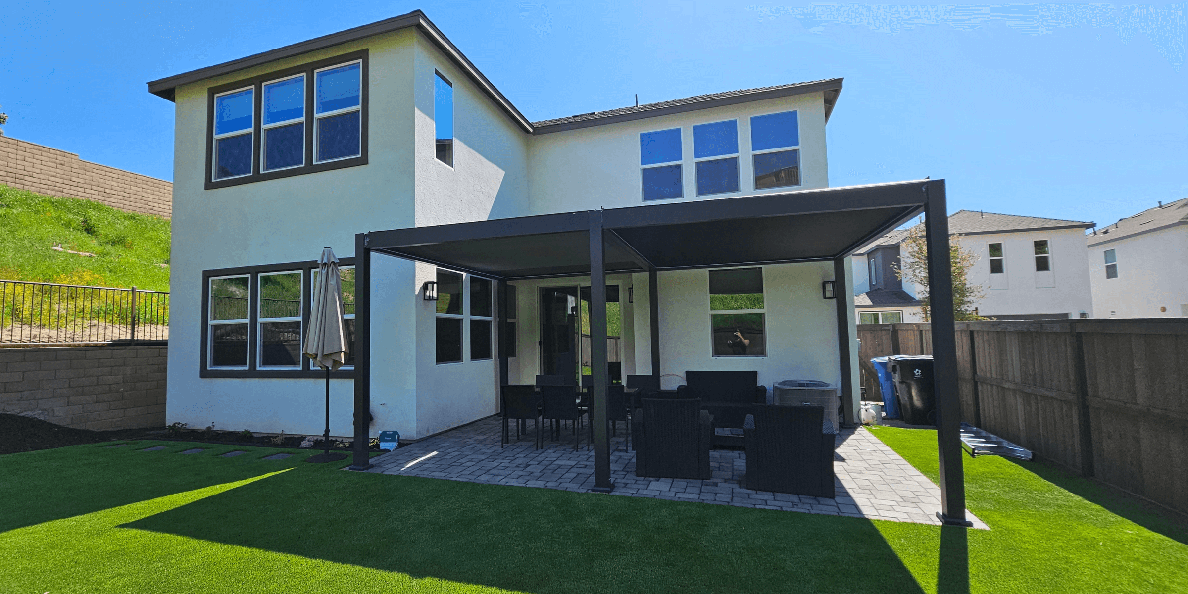 A black pergola outside a white house with a green manicured lawn